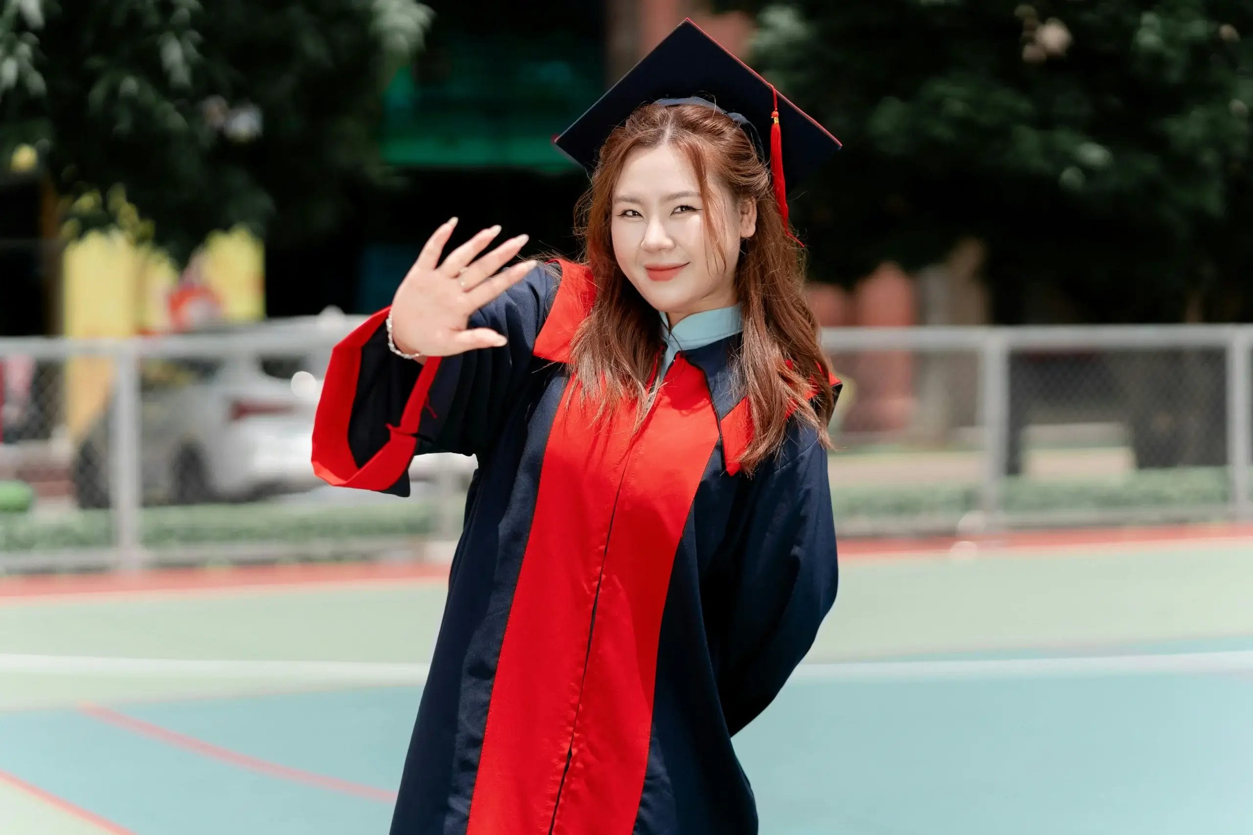 Smiling Graduate Waving in Cap and Gown Outdoors